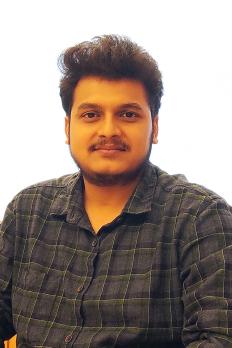 headshot of Nanda wearing grey plaid