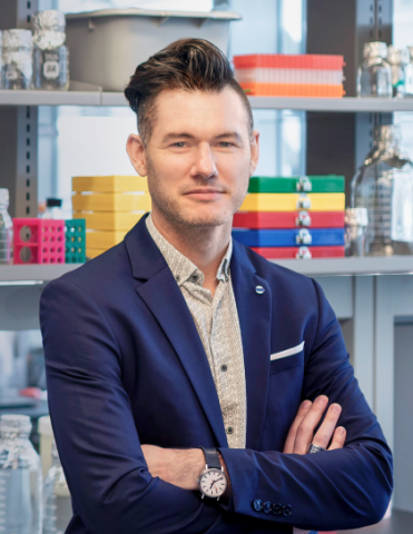 Photo of Shane Liddelow in blue jacket standing in a lab